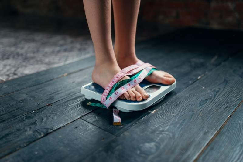womans-feet-on-the-scales-tied-with-measuring