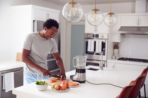man wearing pyjamas standing in kitchen chopping fruit and vegetables for fresh smoothie